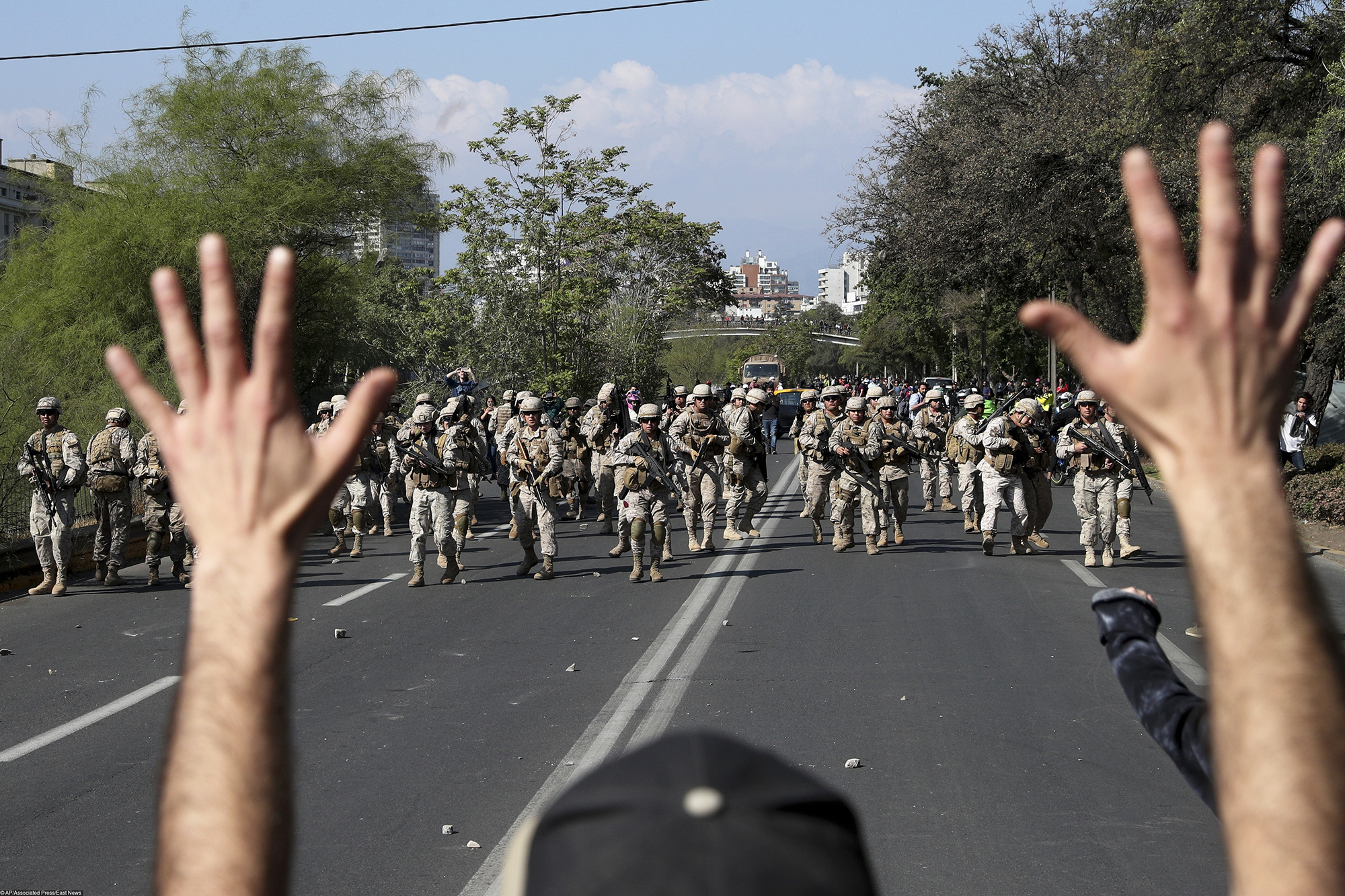 Протестующий против силовиков в Сантьяго A demonstrator holds up his hands toward advancing soldiers as a state of emergency remains in effect in Santiago, Chile, Sunday, Oct. 20, 2019. Protests in the country have spilled over into a new day, even after President Sebastian Pinera cancelled the subway fare hike that prompted massive and violent demonstrations