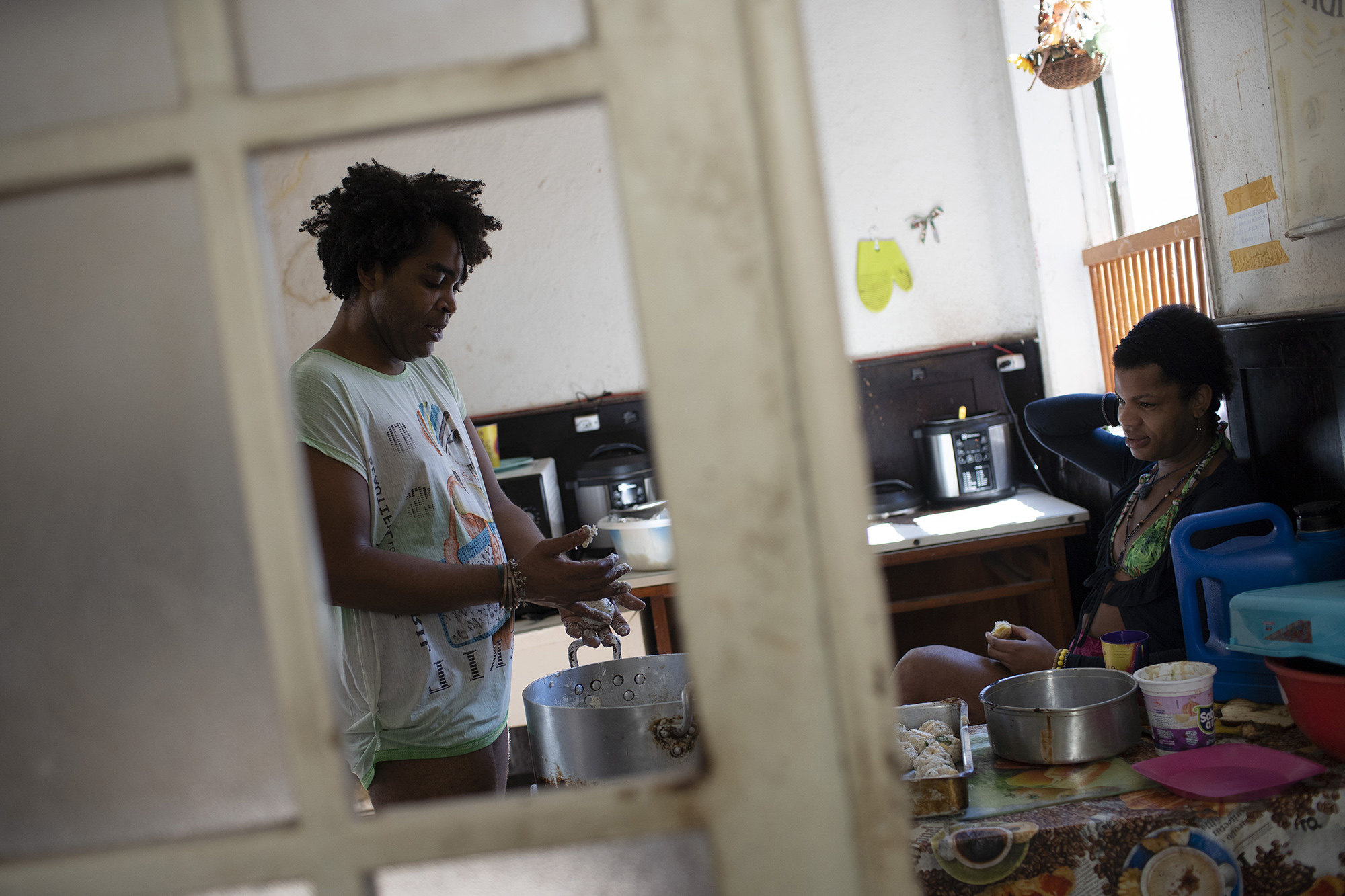 Morgana keeps Micaela company as she prepares rice balls for lunch in the kitchen of the squat known as Casa Nem, occupied by members of the LGBTQ community who are in self-quarantine as a protective measure against the new coronavirus, in Rio de Janeiro, Brazil, Wednesday, July 8, 2020. Self-imposed lockdown is one of few ways this traditionally marginalized group has found to minimize COVID-19 risks, while others remain vulnerable on the streets.