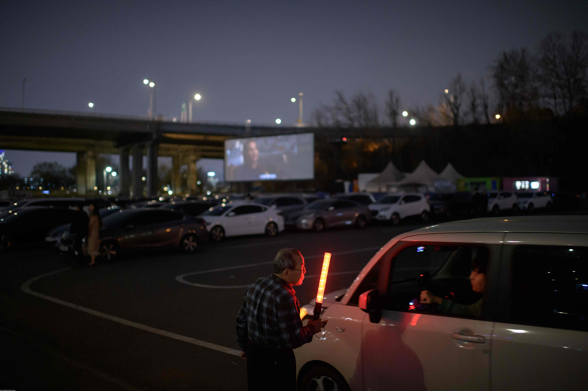Билетер руководит движением на парковке drive-in кинотеатра в Сеуле. Билетер руководит движением на парковке drive-in кинотеатра в Сеуле.